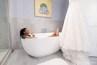 Bride clothed in bathtub sipping champagne