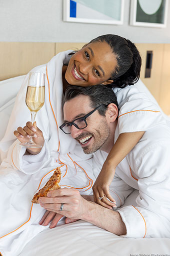Bride and groom in robes holding a glass of champagne and a slice of pizza