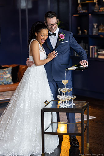 bride hugging groom as he pours champagne into a tower of champagne coupes