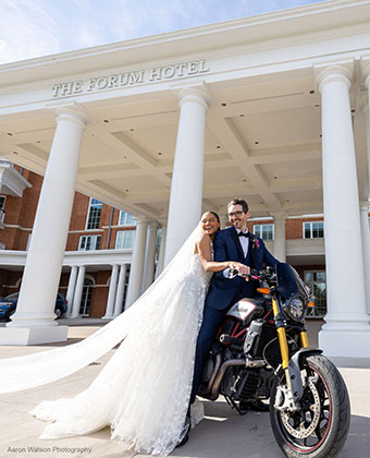 a newlywed bride and groom off on a motorcycle in front of The Forum Hotel